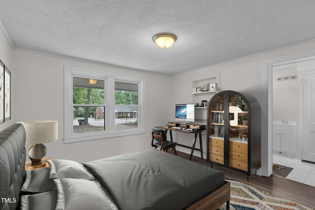 bedroom with wood finished floors, a textured ceiling, ornamental molding, and ensuite bathroom