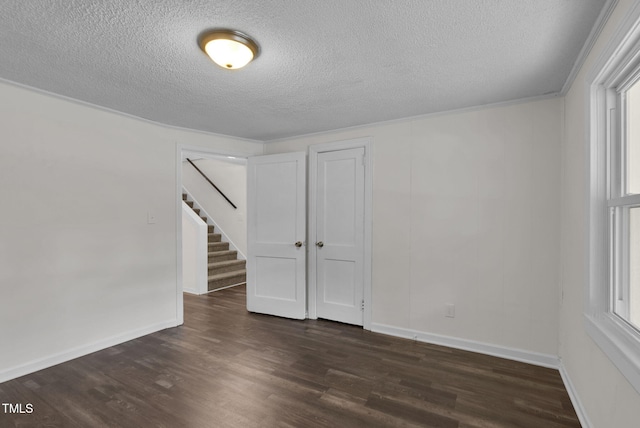 empty room with a textured ceiling, dark wood-style floors, baseboards, and stairs