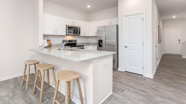 kitchen with light hardwood / wood-style flooring, white cabinetry, stainless steel appliances, a kitchen bar, and kitchen peninsula