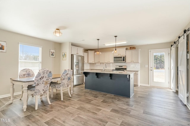 kitchen with light stone counters, appliances with stainless steel finishes, an island with sink, pendant lighting, and a barn door