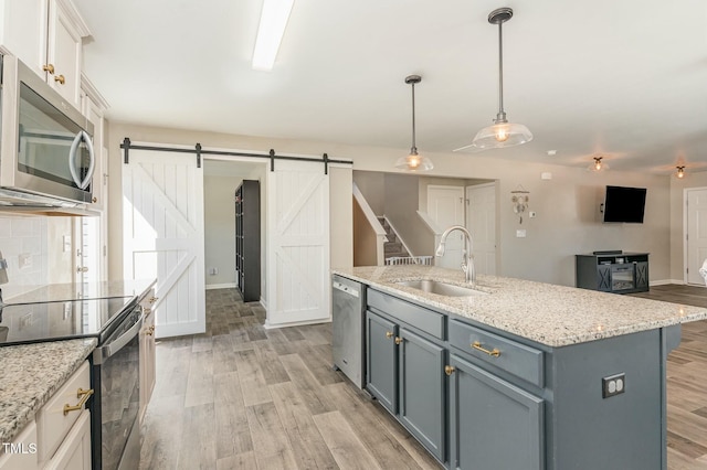 kitchen featuring sink, white cabinetry, stainless steel appliances, a barn door, and a kitchen island with sink