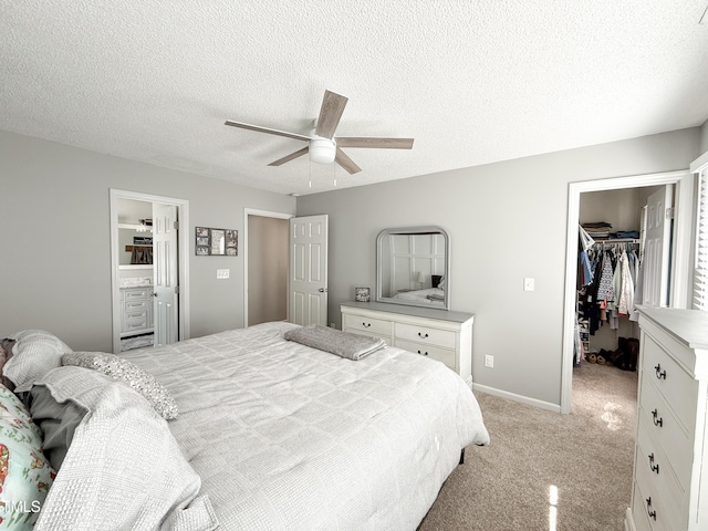 bedroom with a walk in closet, light colored carpet, a textured ceiling, a closet, and ceiling fan