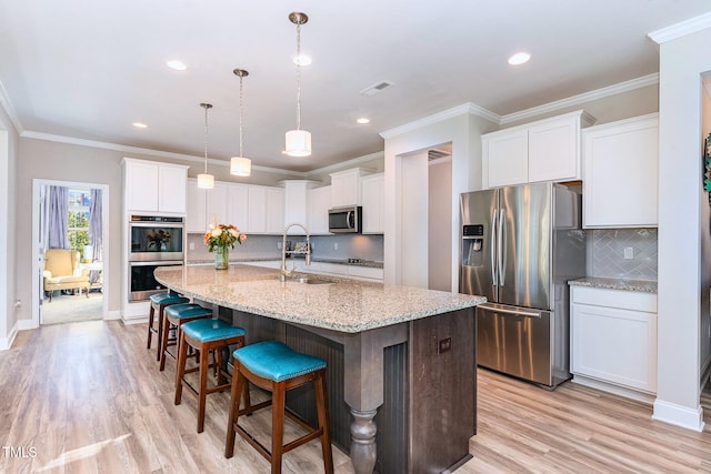 kitchen featuring appliances with stainless steel finishes, pendant lighting, white cabinetry, an island with sink, and sink