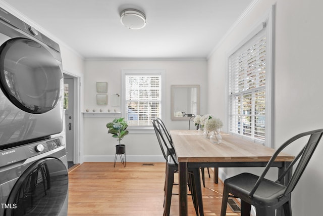 dining room featuring crown molding, plenty of natural light, stacked washing maching and dryer, and light hardwood / wood-style flooring