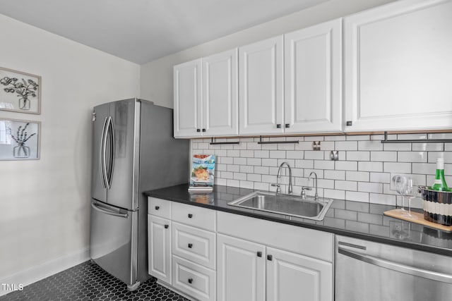 kitchen featuring sink, appliances with stainless steel finishes, dark tile patterned floors, decorative backsplash, and white cabinets