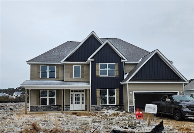 craftsman house with stone siding, roof with shingles, an attached garage, covered porch, and board and batten siding