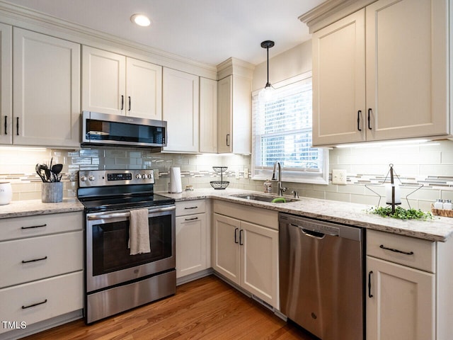 kitchen with sink, pendant lighting, stainless steel appliances, light hardwood / wood-style floors, and decorative backsplash