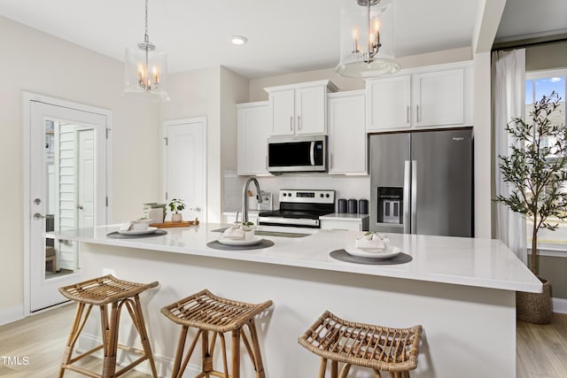 kitchen featuring white cabinetry, stainless steel appliances, hanging light fixtures, and a center island with sink