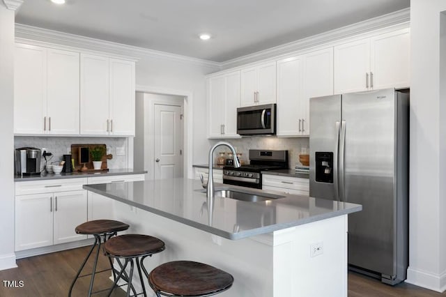 kitchen with sink, stainless steel appliances, an island with sink, white cabinets, and a kitchen bar