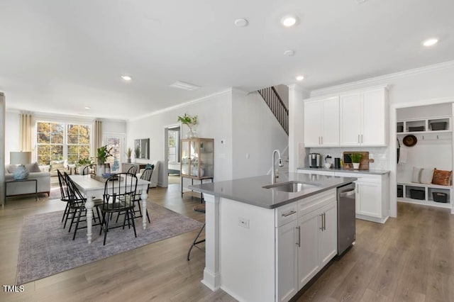 kitchen with sink, wood-type flooring, stainless steel dishwasher, a kitchen island with sink, and white cabinets