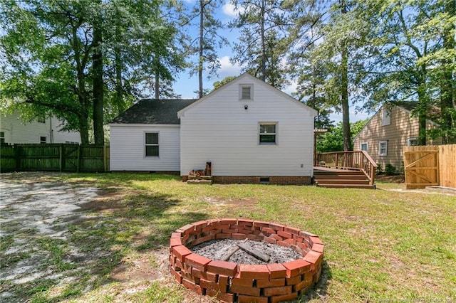 rear view of house with an outdoor fire pit, a deck, and a lawn