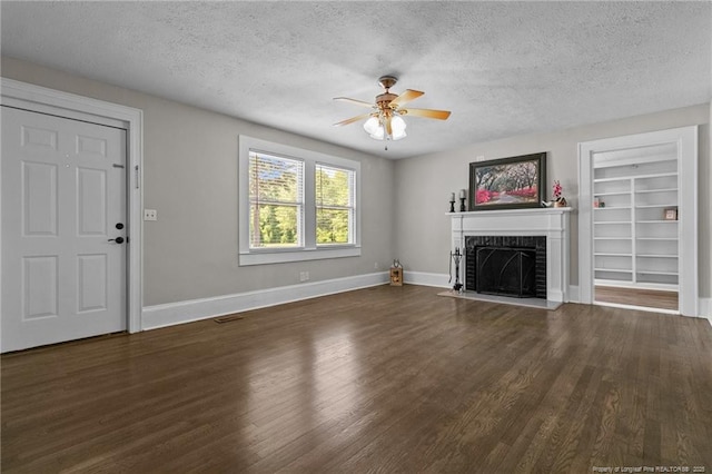 unfurnished living room featuring a brick fireplace, dark wood-type flooring, a textured ceiling, and ceiling fan