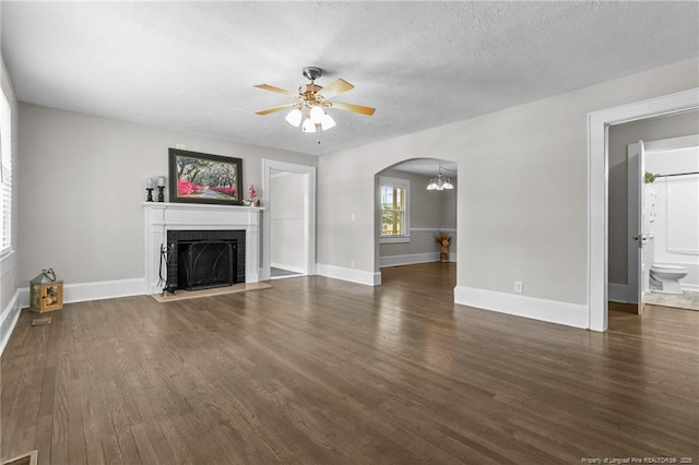 unfurnished living room featuring dark hardwood / wood-style floors, ceiling fan with notable chandelier, a brick fireplace, and a textured ceiling