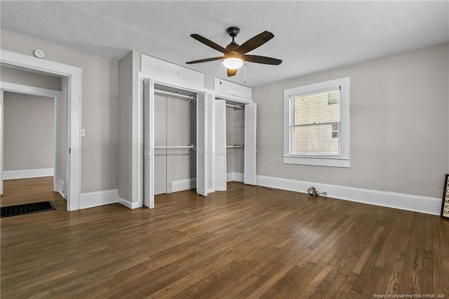 unfurnished bedroom featuring dark wood-type flooring, ceiling fan, a textured ceiling, and two closets