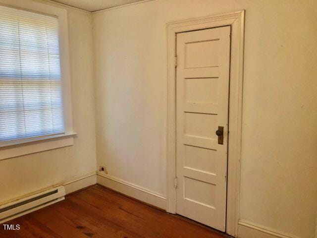 unfurnished room featuring a baseboard radiator, baseboards, and dark wood-type flooring