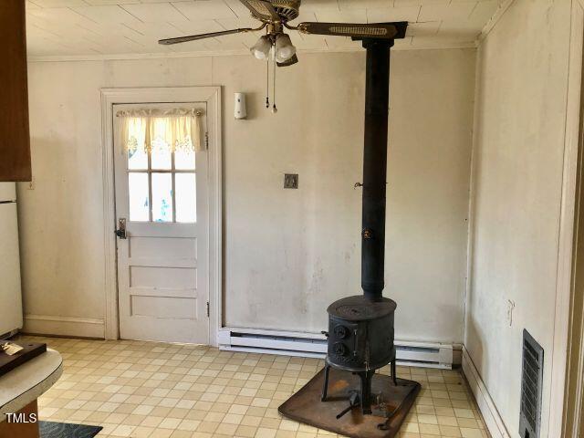 doorway featuring ornamental molding, baseboard heating, a wood stove, and a ceiling fan