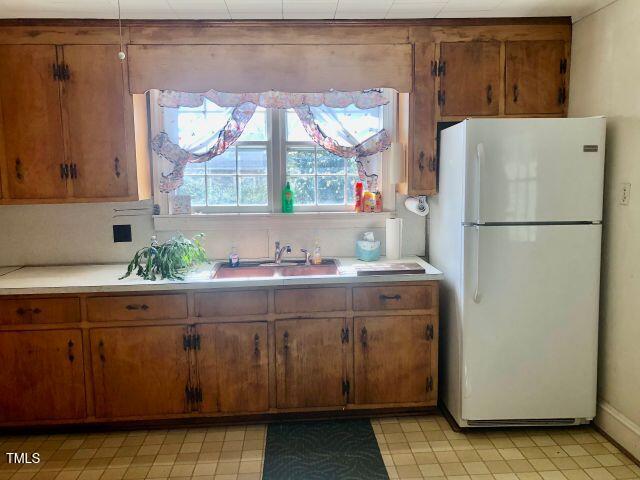 kitchen with brown cabinetry, freestanding refrigerator, light countertops, and a sink