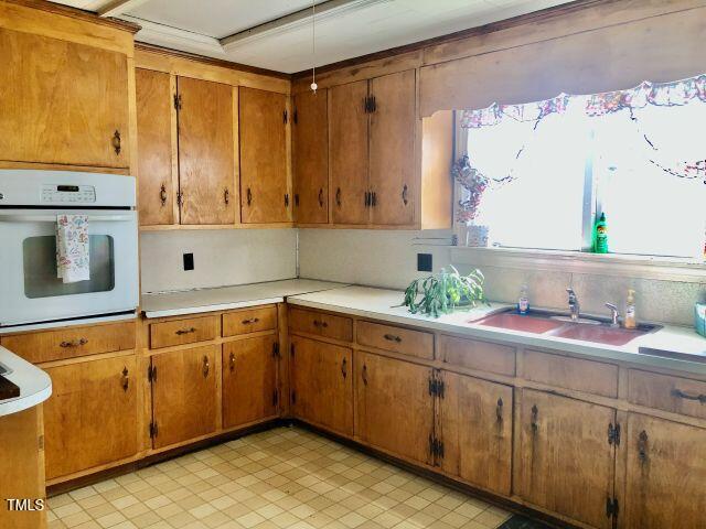 kitchen with brown cabinets, light countertops, a sink, and white oven