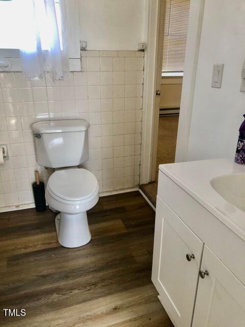 bathroom featuring a baseboard radiator, toilet, wood finished floors, vanity, and tile walls