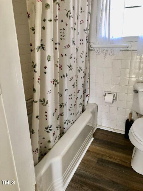 bathroom with toilet, shower / tub combo, tile walls, and wood finished floors