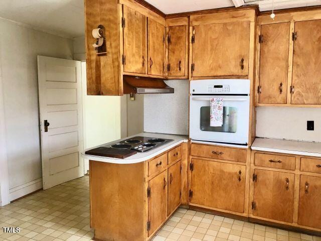 kitchen with oven, a peninsula, stainless steel electric cooktop, light countertops, and brown cabinets