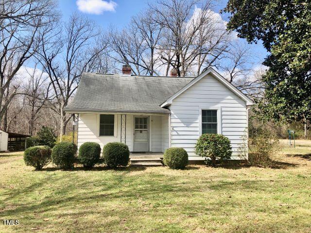 view of front of property with covered porch, a chimney, and a front lawn