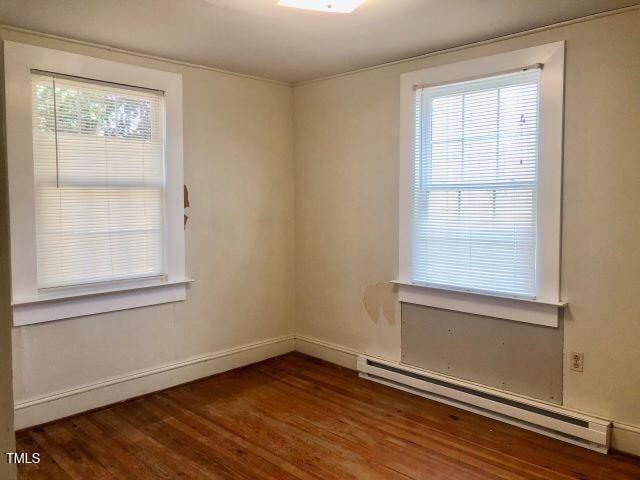 spare room with a baseboard heating unit, baseboards, wood finished floors, and a healthy amount of sunlight