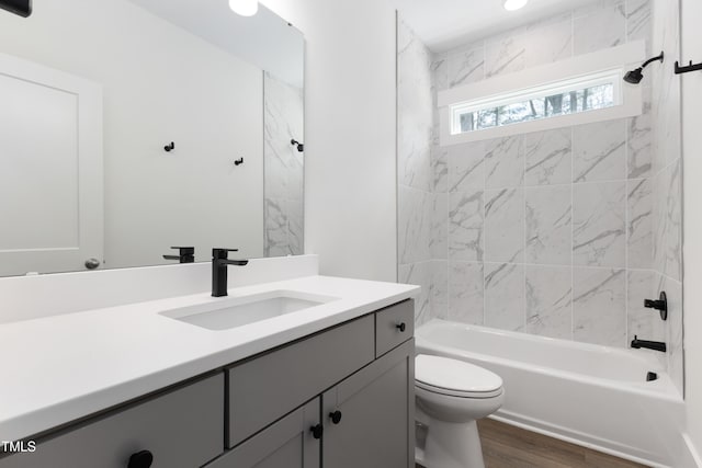 full bathroom with tiled shower / bath combo, vanity, hardwood / wood-style flooring, and toilet