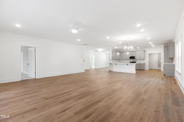 unfurnished living room featuring ceiling fan with notable chandelier and light hardwood / wood-style flooring