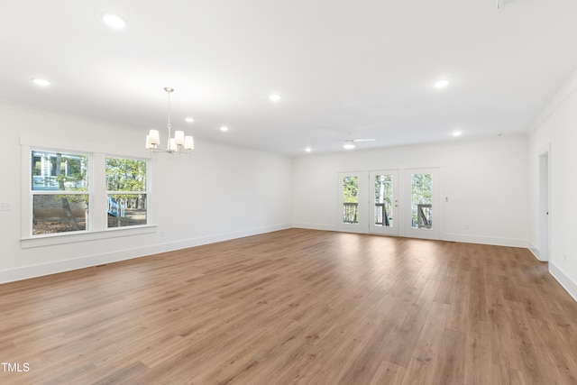 unfurnished living room with ceiling fan with notable chandelier, crown molding, and light hardwood / wood-style floors