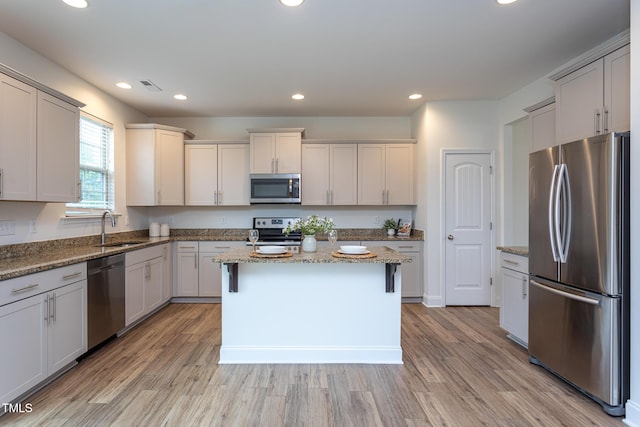 kitchen featuring sink, stainless steel appliances, a center island, light hardwood / wood-style floors, and light stone countertops