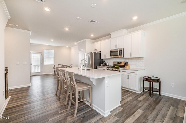 2708 Chert Ln, Raleigh, NC 27610 - kitchen with stainless steel appliances, a center island with sink, ornamental molding, dark wood finished floors, and backsplash