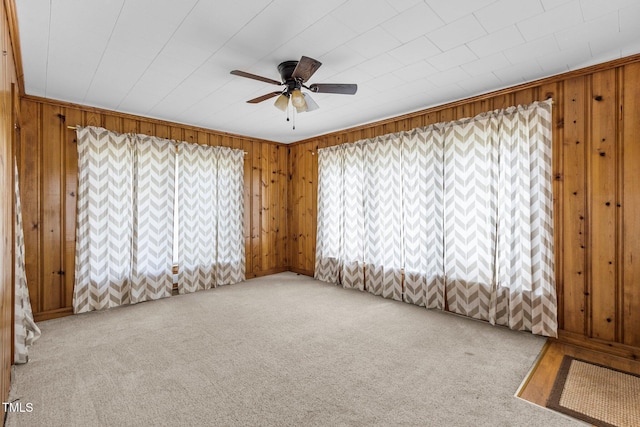 empty room featuring ceiling fan, carpet flooring, and wood walls