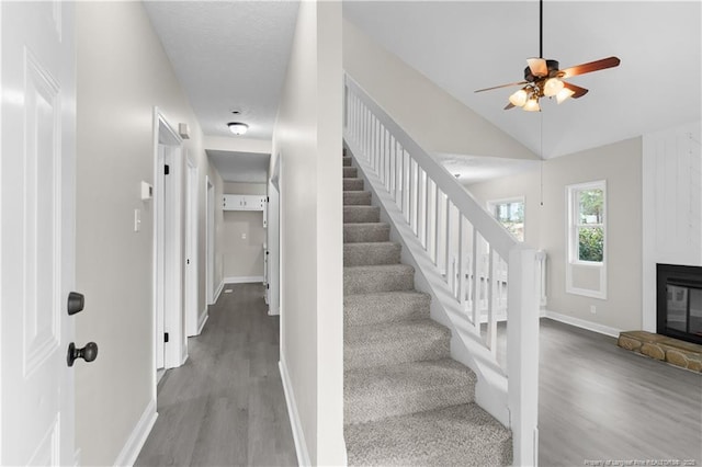 stairway with a stone fireplace, wood-type flooring, ceiling fan, and vaulted ceiling