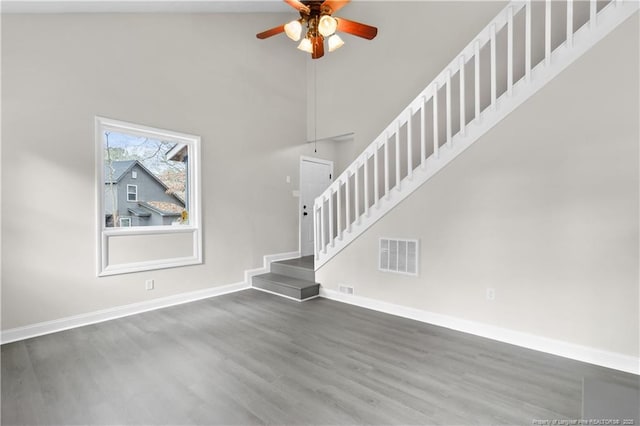 unfurnished living room featuring hardwood / wood-style floors, a towering ceiling, and ceiling fan