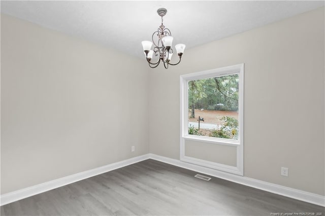 spare room featuring an inviting chandelier and dark wood-type flooring