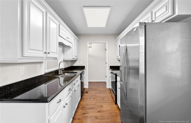 kitchen featuring appliances with stainless steel finishes, white cabinetry, sink, dark stone counters, and light hardwood / wood-style floors