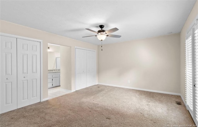 unfurnished bedroom with ceiling fan, ensuite bath, light carpet, and two closets