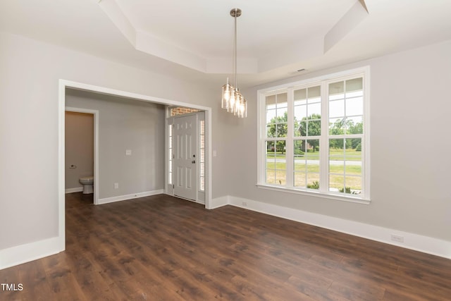 spare room featuring a raised ceiling, dark wood-type flooring, and a chandelier