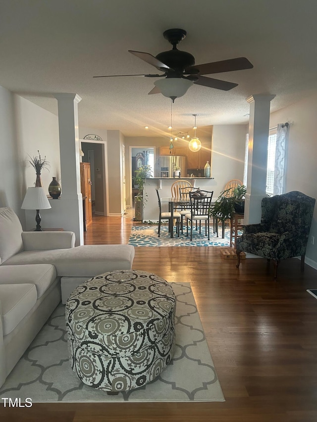 living room featuring hardwood / wood-style flooring, ceiling fan, decorative columns, and a textured ceiling