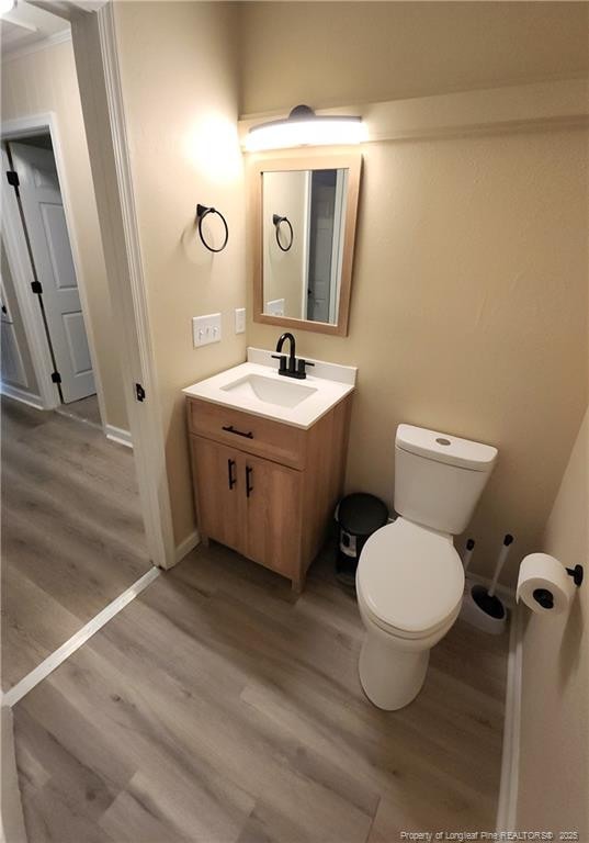 bathroom with crown molding, wood-type flooring, toilet, and vanity