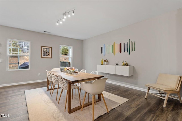 dining area with dark wood-type flooring and track lighting