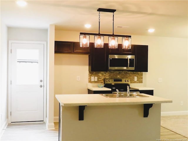 kitchen with appliances with stainless steel finishes, pendant lighting, tasteful backsplash, an island with sink, and sink