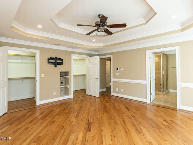 unfurnished bedroom with multiple closets, a tray ceiling, light hardwood / wood-style floors, and crown molding