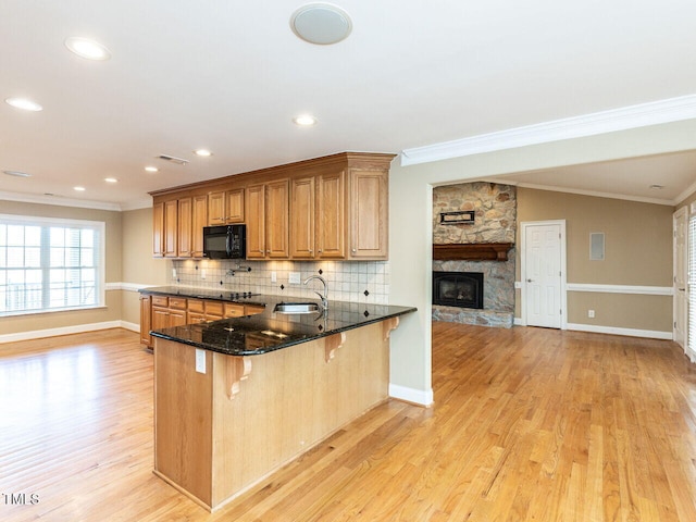 kitchen with a breakfast bar, sink, dark stone counters, kitchen peninsula, and light hardwood / wood-style flooring