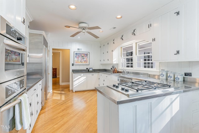 kitchen with stainless steel appliances, white cabinetry, ceiling fan, and light wood-type flooring