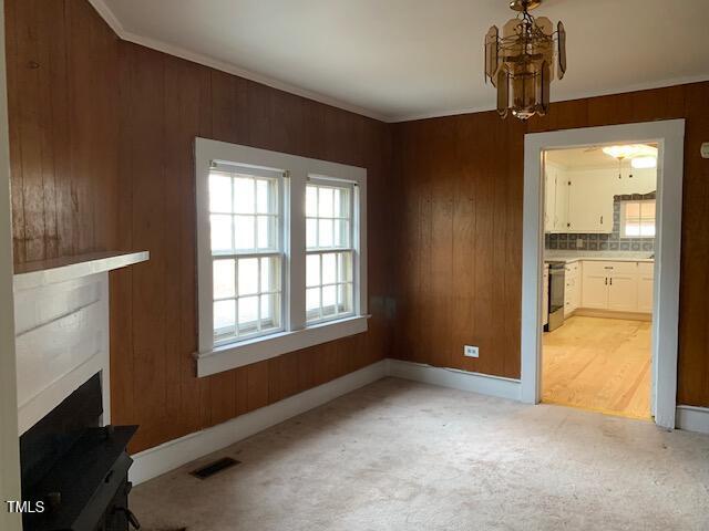 unfurnished living room with light colored carpet, wooden walls, and a chandelier