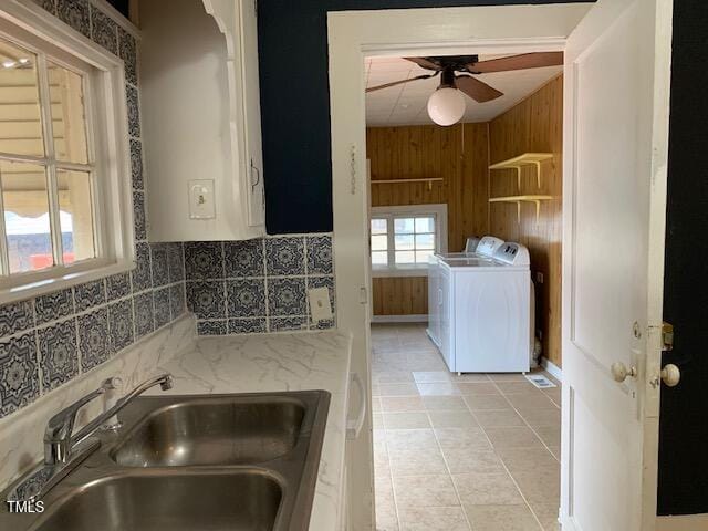 kitchen featuring wooden walls, sink, light tile patterned floors, light stone counters, and ceiling fan