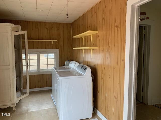 clothes washing area with light tile patterned floors, washer and dryer, and wood walls