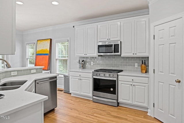 kitchen with sink, white cabinetry, stainless steel appliances, ornamental molding, and light wood-type flooring